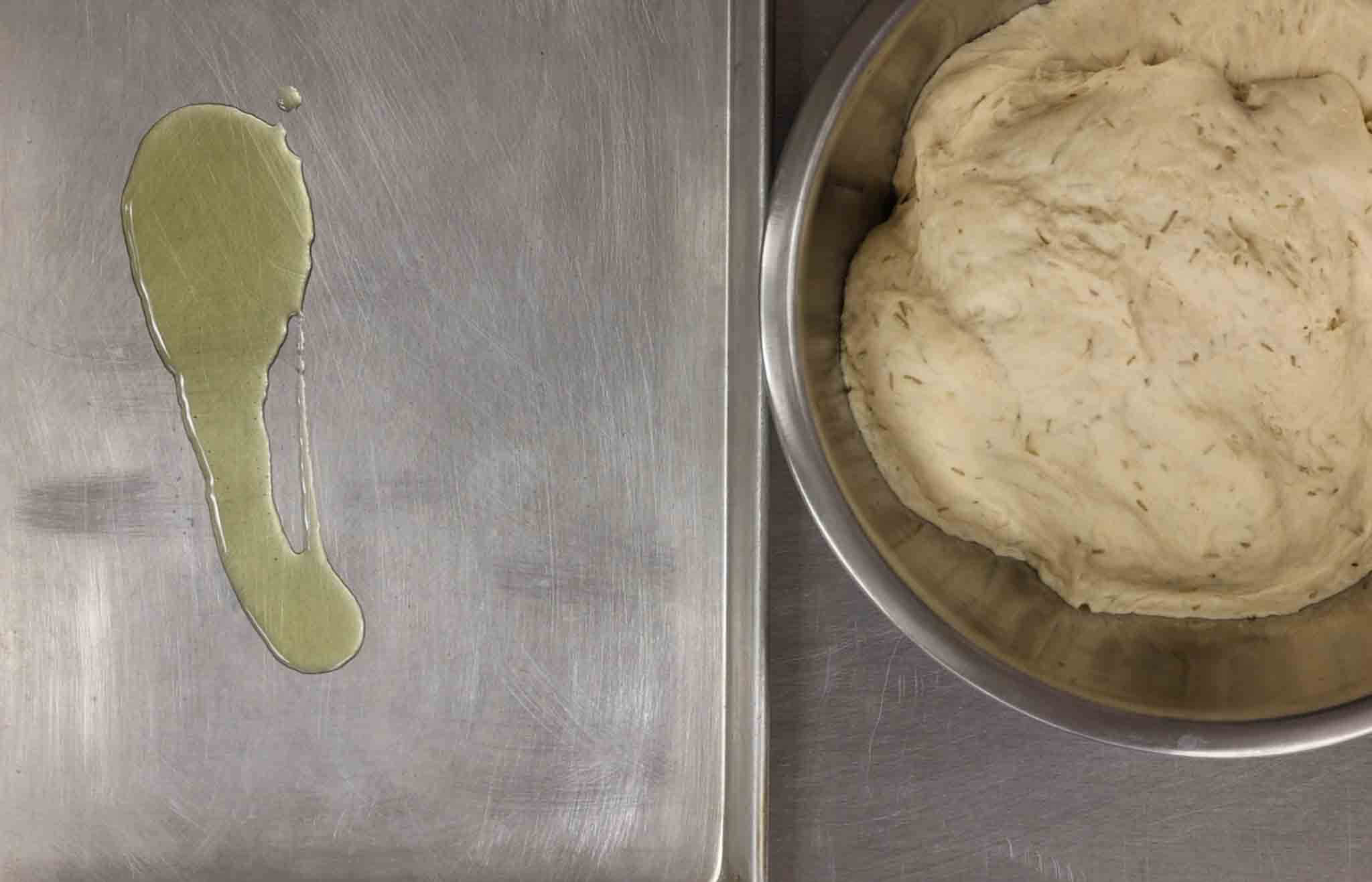 oiled baking sheet and risen rosemary focaccia dough